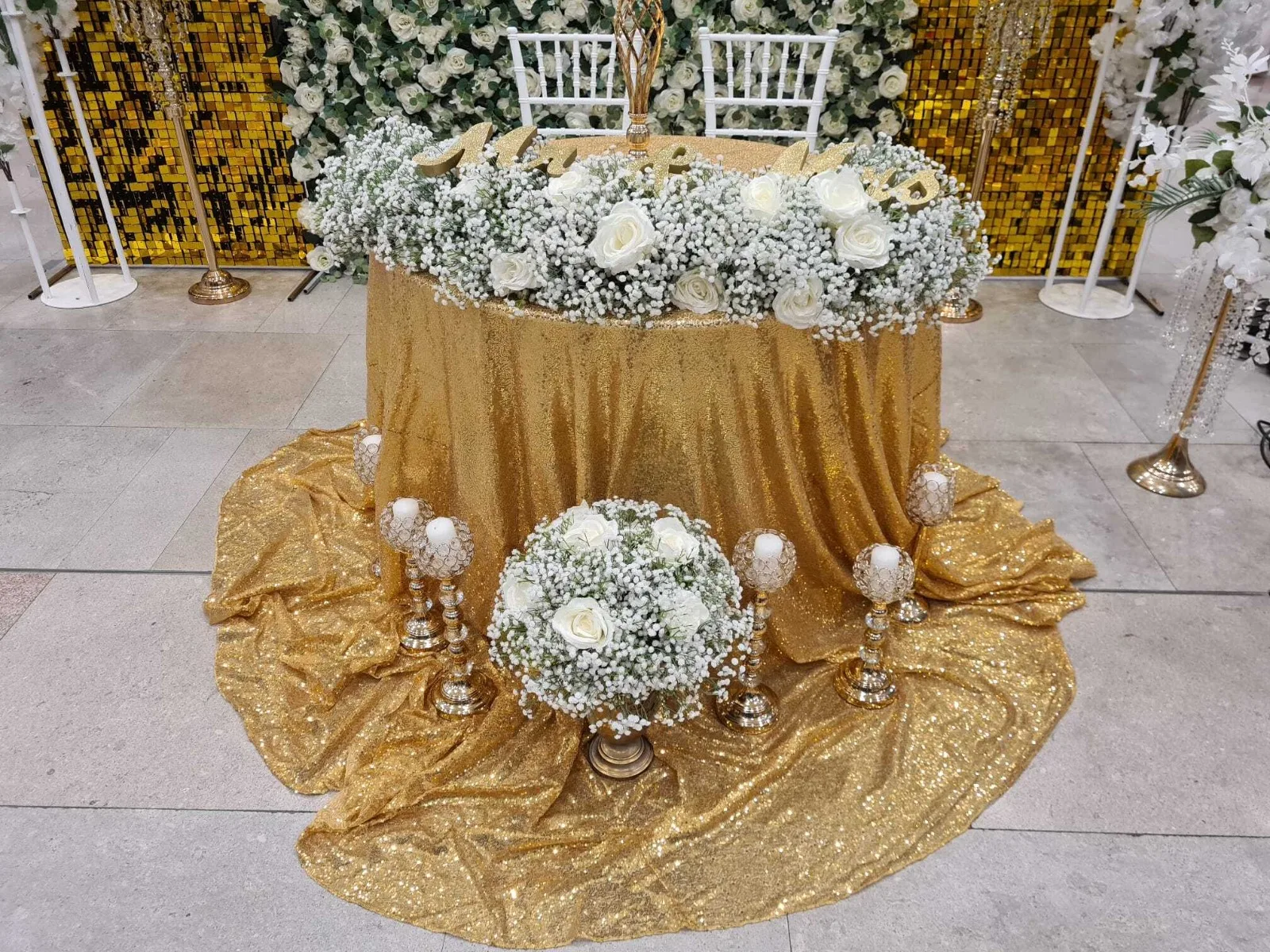 Masa rotunda cu fata de masa aurie si aranjament floral alb cu bujori la targul de nunti