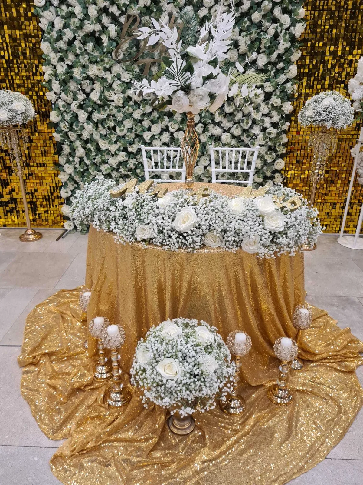 Perete floral verde-alb cu scaune albe tip Chiavari si masa aurie cu flori la targul de nunti