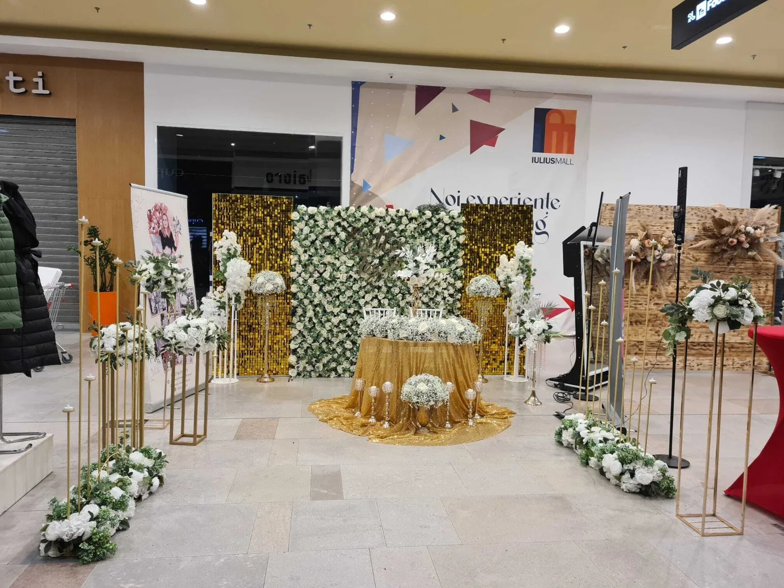 Perete floral, masa aurie si stative aurii cu aranjamente de flori albe la standul de la targul de nunti