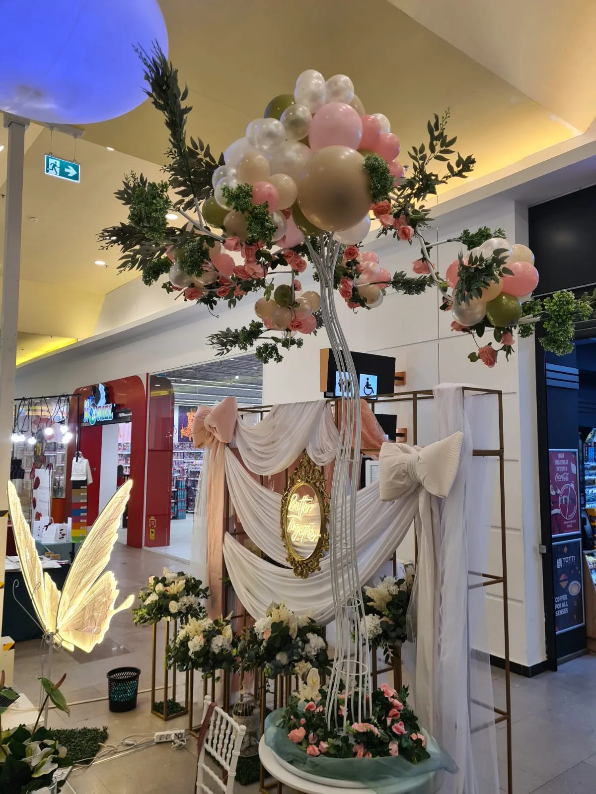 Arcada florala cu baloane roz si albe la intrarea standului, intr-un mall