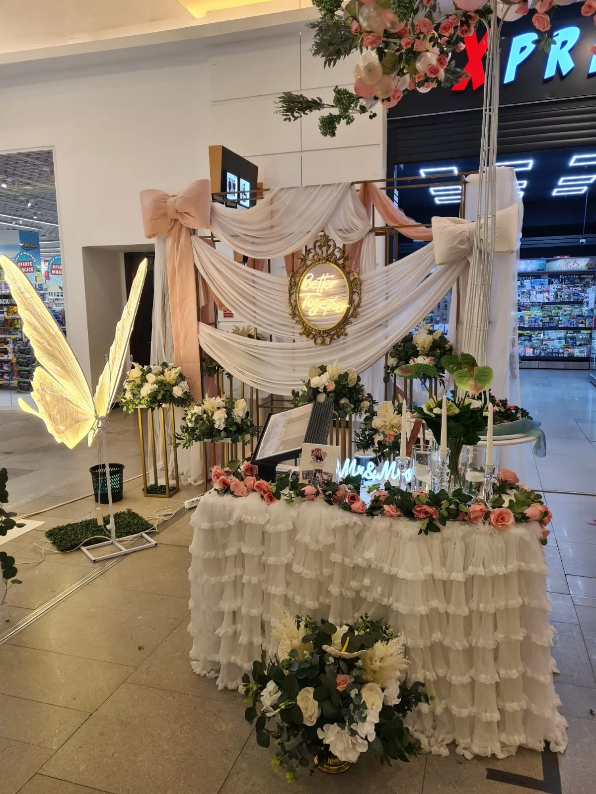 Aripi de fluture luminoase langa arcada si masa decorata cu flori, la targul de nunti